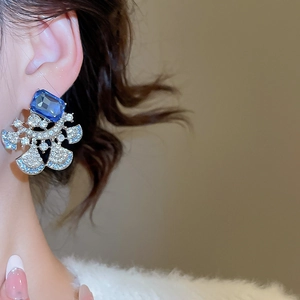 Close-up of elegant silver earrings with rectangular blue stone and fan-shaped crystals