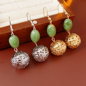 Detailed shot of hollow filigree metal ball earrings with green beads in gold and silver