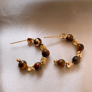 Gold C-shaped earrings with tiger eye beads and silver pins on a grey fabric background