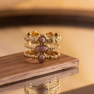 Detail of gold-plated multi-layer ring with pink oval gemstones on a wooden surface