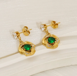 Detail of gold-plated rose earrings with green gemstone and zircon accents on white fabric