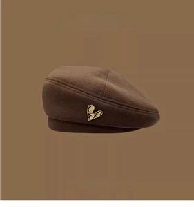 Detail of dark brown wool beret featuring a golden heart metal emblem on fabric