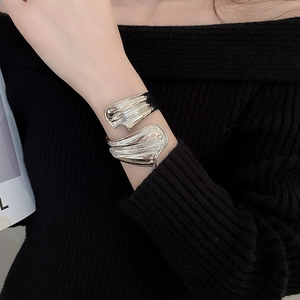 Detailaufnahme einer silbernen unregelmäßigen Manschette mit gewellter Metalltextur