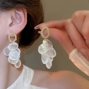Close-up of elegant gold round shell tassel earrings worn on ear showing texture