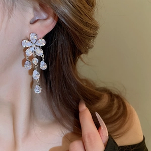 Close-up of elegant flower stud earrings with hanging teardrop tassels on female model