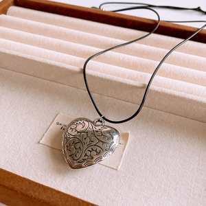 Detailed view of an antique heart pendant with vine engraving on a black wax cord