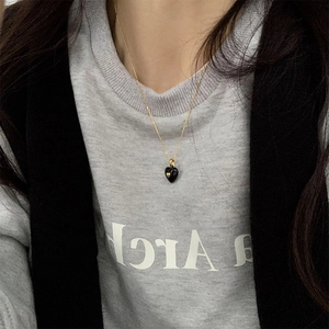 Close-up of a vintage black heart pendant necklace with gold detail on a female model