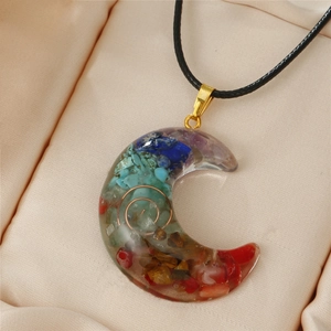 Macro shot of a crescent moon resin pendant with chakra stones on pink silk fabric