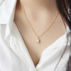 Detailed view of an irregular baroque pearl pendant on a gold twisted rope chain necklace