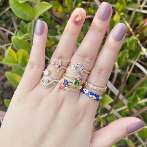 Gold rings set with colorful zircons, evil eye and heart charms worn by female model