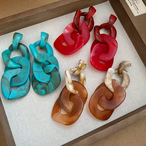 Detailed view of colorful acrylic chain drop earrings on a rustic wooden tray display