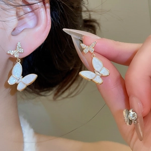 Macro shot of elegant zircon butterfly earrings featuring pearl white enamel and gold trim