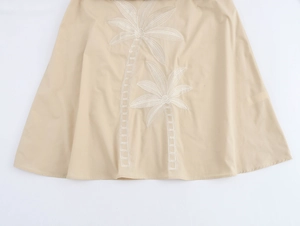 Gros plan de la broderie de cocotier sur la jupe beige avec détails de couture