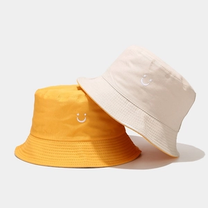Detailed close-up of yellow and beige cotton bucket hats with minimalist smile embroidery