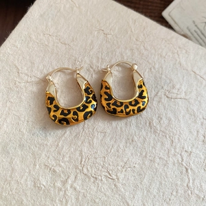 Detailed view of U-shaped gold earrings featuring classic leopard print enamel finish