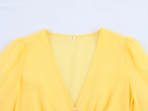 Detail of yellow V-neck chiffon dress with delicate lace stitching and pearl buttons