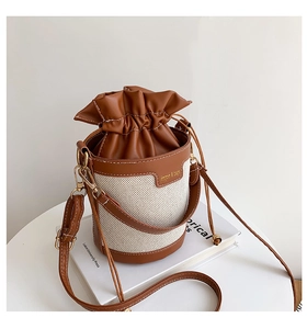 Detail of a brown leather and beige canvas bucket bag with drawstring closure and logo patch