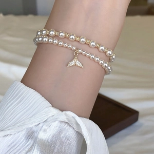 Close-up of double-layer pearl bracelet with a sparkling zircon fishtail charm on wrist