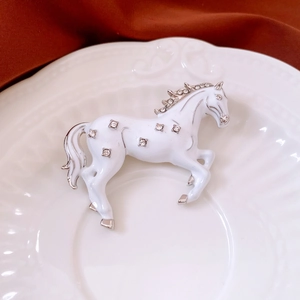 Close-up of a white enamel horse brooch with sparkling rhinestones on a ceramic plate