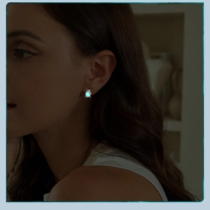 Glow-in-the-dark owl stud earring emitting bright cyan light in dark setting
