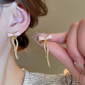 Detail of pink bow earrings with gold tassels and crystals on a model side view