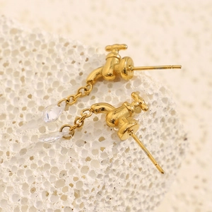 Macro shot of 18K gold faucet earrings with a clear teardrop crystal on a stone texture