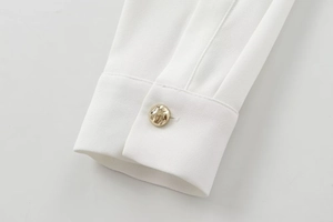 Detailed close-up of white crepe fabric cuff with an ornate embossed gold button