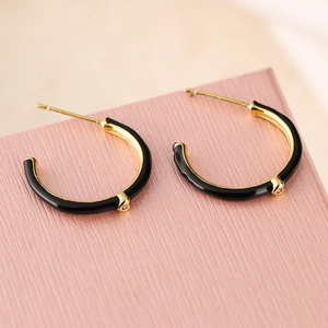 Detail of C-shaped black enamel earrings with gold trim on a pink textured base