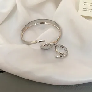 Polished silver minimalist snake-style open bracelet and ring set on white satin