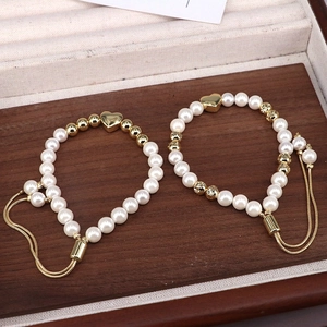 Detail of adjustable pearl bracelets with gold heart charms on a wooden surface