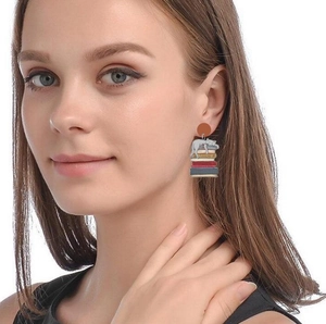 Acrylic sleeping cat on colorful books earrings worn by a model in a studio setting