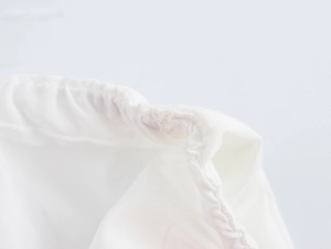 Detailed close-up of drawstring channel and stitching on a white woven fabric bag