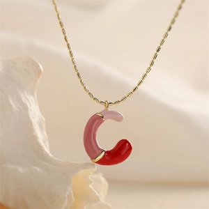 Détail du pendentif lettre C en émail rose et rouge sur une chaîne de collier dorée