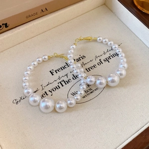 Irregular crossover gold hoop earrings featuring a gradient pearl arrangement design