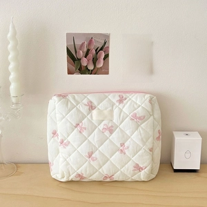 Detailed view of white quilted cosmetic bag with pink bow pattern on a wooden desk