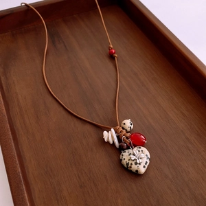 Détail du pendentif en pierre de cœur avec perles de coquillage et verre sur cordon