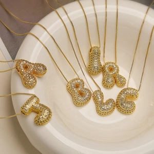 Gold-plated initial letter necklaces with clear crystals displayed in a white ceramic bowl