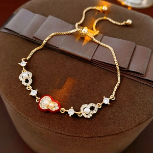 Detail of gold-plated bracelet featuring red heart pendant, pearls, and adjustable box chain