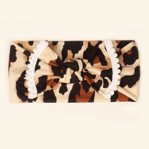 Detail of leopard print baby headband featuring bow design and white pom pom trim