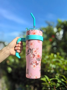 Detail of pink floral 40oz insulated tumbler with turquoise handle in outdoor setting