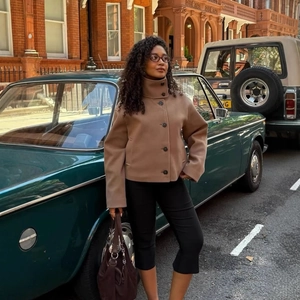 Women's brown stand collar cropped wool jacket paired with black trousers in city setting