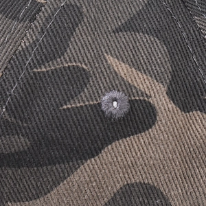 Gros plan de l'œillet d'aération brodé sur le tissu sergé camouflage de la casquette
