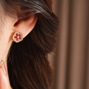 Close-up of golden flower stud earrings with red gemstones and sparkling small diamonds