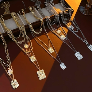 Detail of multi-layered gold and silver square textured necklaces on a wooden display