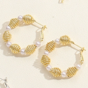 Detailed close-up of gold hoop earrings featuring spiral metal beads and white pearls
