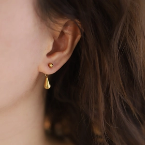 Dettaglio ravvicinato di un orecchino a goccia d'oro minimalista indossato da una modella