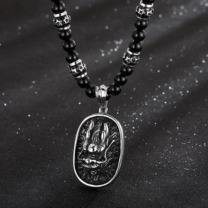 Macro detail of silver dragon relief pendant on punk style black beaded necklace