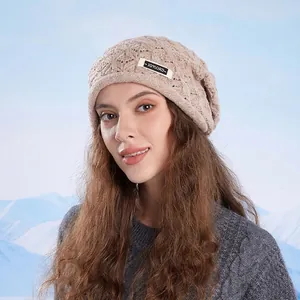 Beige knit beanie with ear protection and brand label against a snowy mountain background