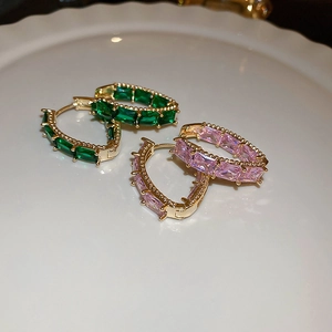 Detailed shot of gold hoop earrings with emerald and pink zircon stones on a white tray