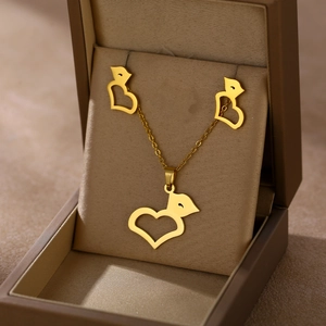 Close-up of gold stainless steel heart and bird necklace jewelry set in a beige velvet box